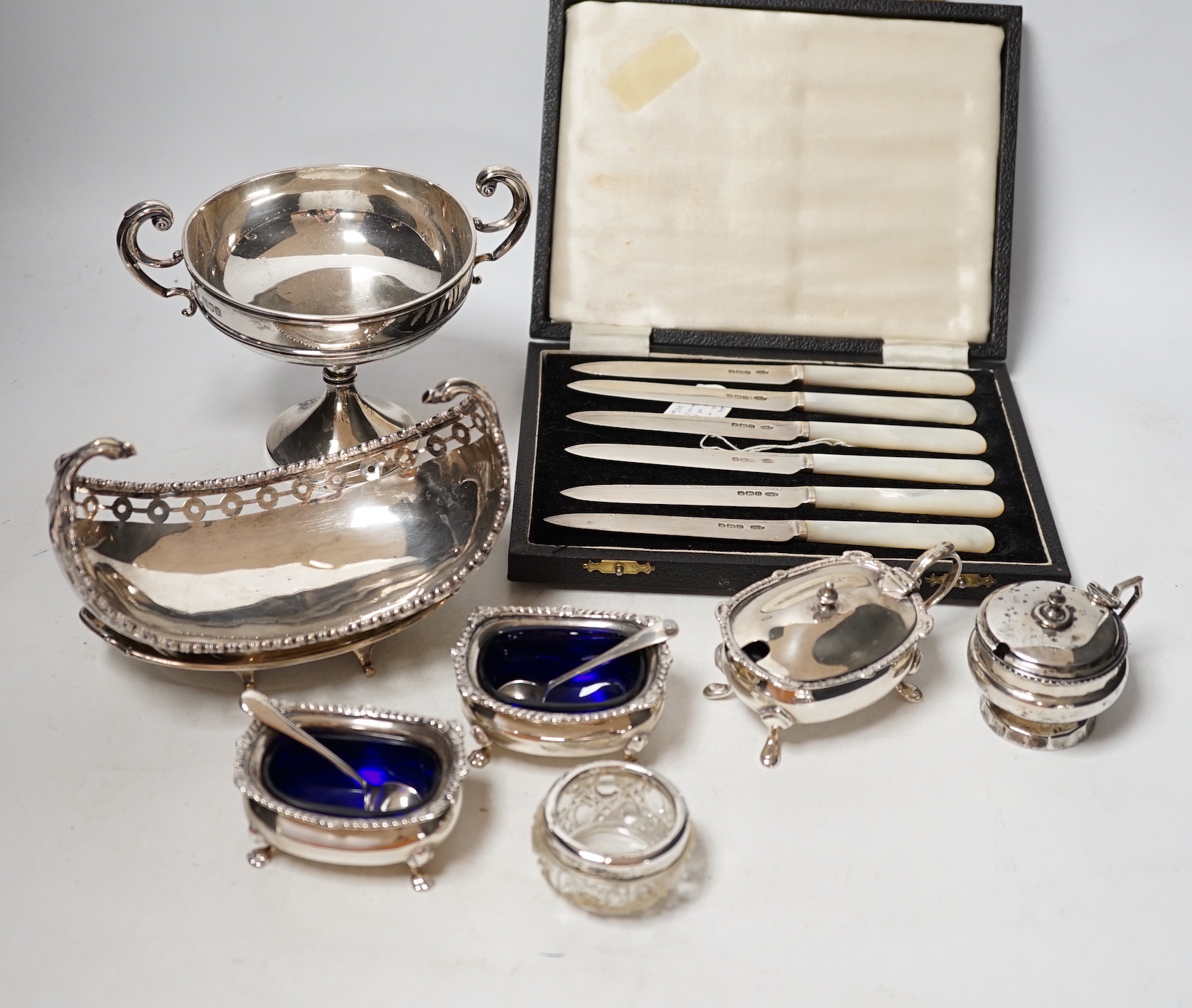 An Edwardian small silver two handled pedestal dish, London, 1902, height 12cm, a silver inkstand base, a silver boat shaped dish (lacking stand), a pair of silver salts with blue glass liners and spoons, three other sil